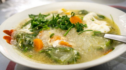 The close up view of the mixed vegetables soup with soo hoon noodles in a bowl.