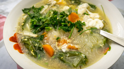 The close up view of the mixed vegetables soup with soo hoon noodles in a bowl.