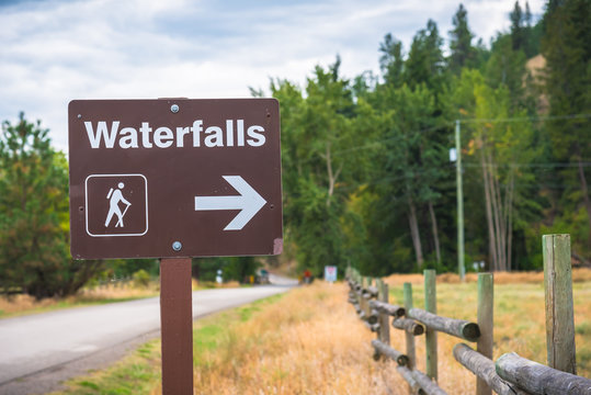 Roadside sign pointing to waterfalls hiking trail with forest in background
