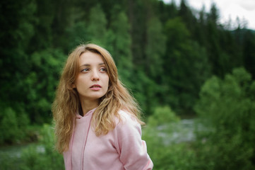 Naklejka premium Amazing young girl in pink casual clothes with long hair on the hill with green forest background during spring or early autumn in the mountains.