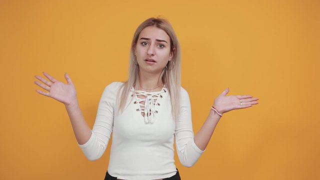 Portrait of serious young woman in casual clothes showing stop gesture with palm isolated on orange wall background in studio. People sincere emotions lifestyle concept.