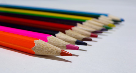 Pencils for drawing lie in a row. The entire palette of colored pencils. Drawing tool. Colored pencils isolated on white background. Blurred background.