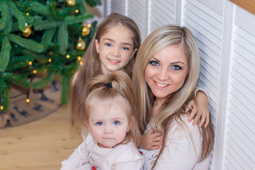 Mom and daughters at the Christmas tree. Christmas season. Sisters. Merry Christmas and happy holidays Cheerful mom and her cute daughters exchange gifts.