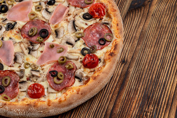 Hot meat pizza with pepperoni, salami, ham, melted cheese and olives on wooden table