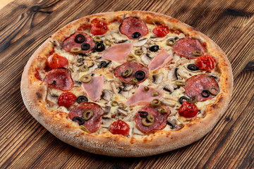 Hot meat pizza with pepperoni, salami, ham, melted cheese and olives on wooden table