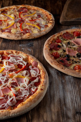 Different pizzas on wooden table in low light