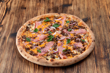 Pizza with minced meat and ham with cheese sauce on wooden table