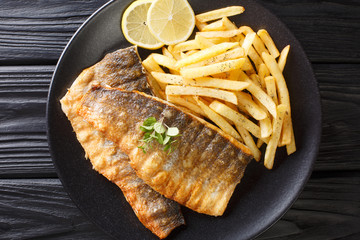 Serving of grilled sea bass fillet with a side dish of french fries close-up on a plate. Horizontal top view