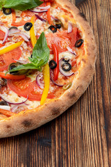 Vegetable pizza with melted cheese, bell pepper, tomatoes and olives on wooden table