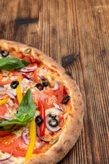 Vegetable pizza with melted cheese, bell pepper, tomatoes and olives on wooden table