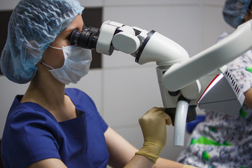 Female dentist looking into a microscope. Treatment of the patient through a microscope in the...