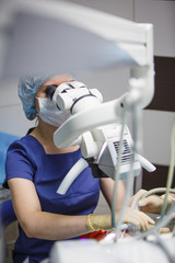 Female dentist looking into a microscope. Treatment of the patient through a microscope in the...
