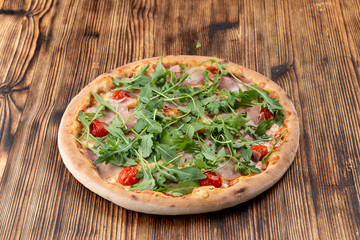 Parma ham pizza with fresh arugula and cherry tomatoes on wooden table