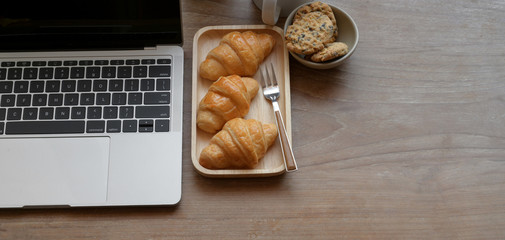 Comfortable workplace with laptop computer and breakfast on wooden table