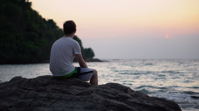 Depressed Sad Young Man Sitting on Rock By The Beach While Staring at Ocean