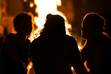 silhouette of group of people sitting in the front of the fire as they talk, seen from behind...