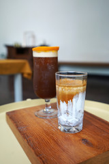 A glass of latte and iced black orange coffee on wooden tray