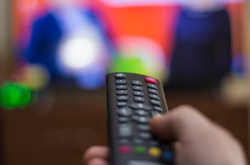 Hand holding TV remote control with TV in background