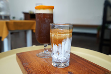 A glass of latte and iced black orange coffee on wooden tray
