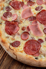 Close up of meat pizza with sausages, pepperoni, spicy chorizo and melted cheese on wooden table