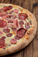 Close up of meat pizza with sausages, pepperoni, spicy chorizo and melted cheese on wooden table