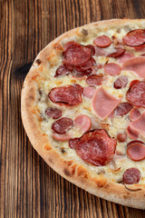 Italian meat pizza with sausages, pepperoni, spicy chorizo and melted cheese on wooden table