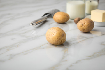 Kartoffeln, Milch, Salz, Butter, Muskatnuss als Zutaten mit Kartoffelpresse und Muskatreibe für Kartoffelpüree auf hell Marmor Hintergrund