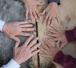 Three pairs of hands touch each other over a wooden table in the forest. Concept of unity and sharing