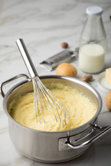 Kochtopf mit Kartoffelpüree mit Zutaten aus Kartoffeln, Milch, Salz, Butter, Muskatnuss dazu Muskatreibe und Schneebesen auf hell Marmor Hintergrund