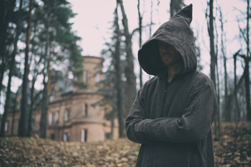 Mysterious monk or wizard in hooded robe stands in forest against the background of medieval castle...