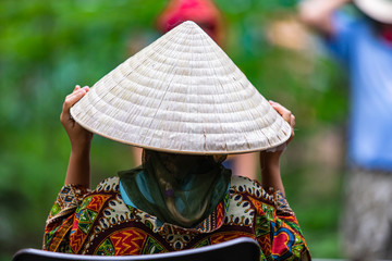 close up and selective focus on a woman wearing Asian conical hat and colorful traditional clothes...