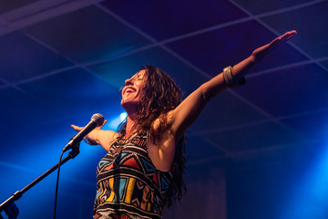 a female musician is viewed from a low angle as she sings and smiling with the audience with her...