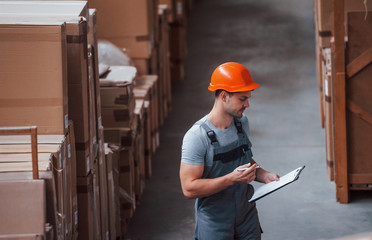 Storage worker in uniform and notepad in hands checks production