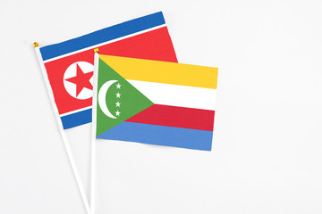 Comoros and North Korea stick flags on white background. High quality fabric, miniature national flag. Peaceful global concept.White floor for copy space.