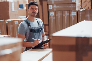 Storage worker in uniform and notepad in hands checks production