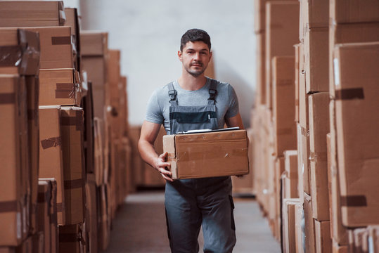 Young male worker in uniform is in the warehouse with box in hands