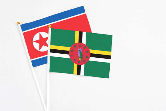 Dominica and North Korea stick flags on white background. High quality fabric, miniature national flag. Peaceful global concept.White floor for copy space.