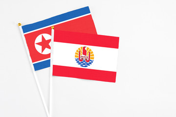 French Polynesia and North Korea stick flags on white background. High quality fabric, miniature national flag. Peaceful global concept.White floor for copy space.