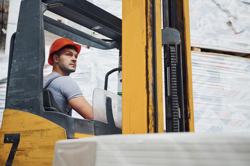 Fototapeta na wymiar Young worker in unifrom sits in the forklift in the warehouse