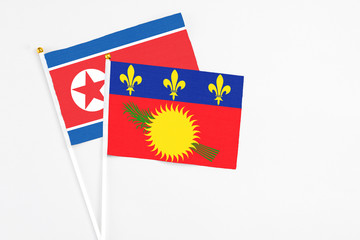 Guadeloupe and North Korea stick flags on white background. High quality fabric, miniature national flag. Peaceful global concept.White floor for copy space.