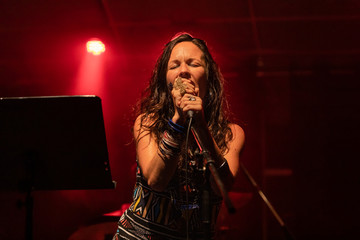 A female musician is viewed from a low angle as she sings with closed eyes during a performance on stage with red lights 