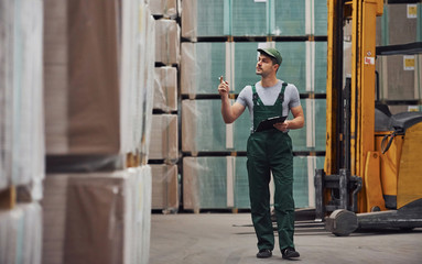 Storage worker in green colored uniform and notepad in hands checks production