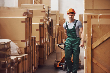 Young male worker in uniform is in the warehouse with pallet truck