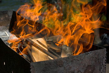 View of a burning fire with a bright flame in the grill on a blurred background of trees