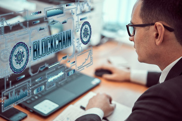Businessman works behind a laptop with a BLOCKCHAIN technology theme hologram. BLOCKCHAIN concept.