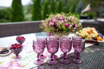 Beautiful glasses of colored purple glass on the table with berries and flowers, composition for catering outdoors