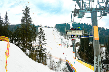 Lift and ski slope with skiers below it on a sunny winter day with blue sky, ski resort Bukovel.