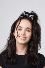 Medium close-up shot of a young brunette European girl with a deep blue textile hair band with golden spots and a light lacy piping. 