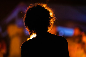 silhouette of an unrecognizable person sitting in the front of the fire, seen from behind during...