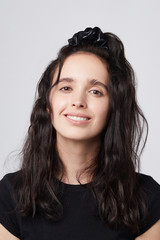 Medium close-up shot of a young brunette European girl with a black textile hair band made of smooth glazy latex fabric. The fashion model with dark wavy hair in a half ponytail is wearing a black top © RedUmbrella&Donkey
